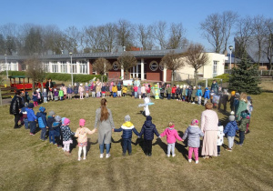 Dzieci stoją w kole w ogrodzie przedszkolnym wokół kukły Marzanny.